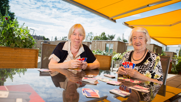 Zwei Bewohnerinnen einer Senioren-WG beim Kartenspielen auf der Terrasse