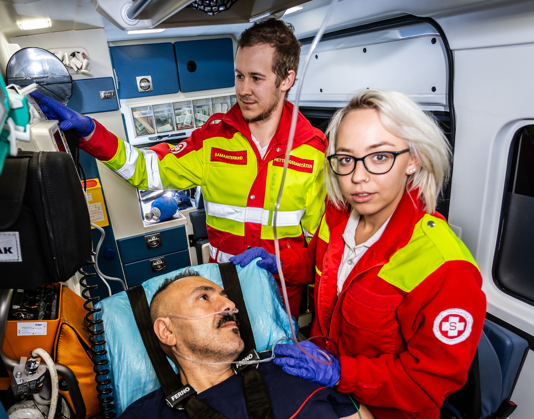 Rettungssanitäterin mit Patienten, Kollege im Hintergrund