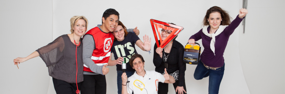Gruppe junger MitarbeiterInnen mit Warndreieck, AED-Schulungsgerät und Stethoskop