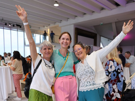 Drei Frauen in bunten Outfits freuen sich gemeinsam in einem festlichen Ambiente.