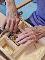 Hände formen Holzspäne in einer Box während einer praktischen Arbeit.