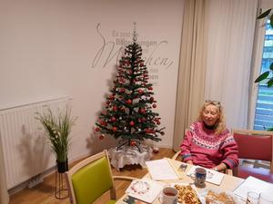 Eine Dame sitzt bei einer Adventsfeier vor einem gedeckten Tisch, links hinter ihr steht ein Christbaum.