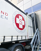 Nahaufnahme LKW mit Samariterbund Logo vor Lagerhalle steht vor Tor um beladen zu werden