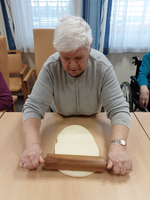 Eine ältere Frau rollt Teig auf einem Tisch aus.