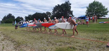 Fünf Athleten stehen bereit mit Surfboards für einen Wettkampf am Wasser.