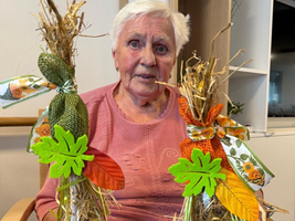 Eine ältere Frau hält zwei dekorativ gestaltete Flaschen mit Herbstmotiven.