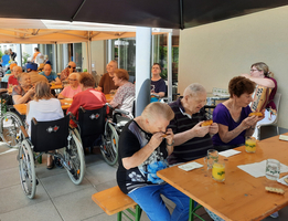 Ältere Menschen sitzen draußen zusammen und genießen Essen und Getränke.