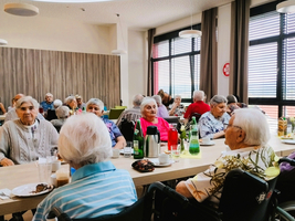 Ältere Menschen sitzen an Tischen in einem hellen Essbereich und unterhalten sich.