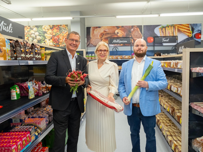 Drei Personen stehen in einem Sozialmarkt zwischen Regalen. Sie halten Lebensmitteln in der Hand. In der Mitte steht die Präsidentin des Samariterbund Wien, Susanne Drapalik.