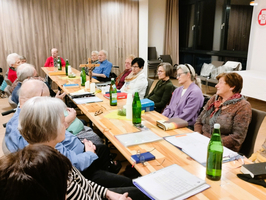 Gruppengespräch mit älteren Menschen an einem Tisch, umgeben von Getränken.