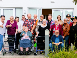 Gruppe von Menschen lächelt und zeigt Daumen hoch vor einem Gebäude.