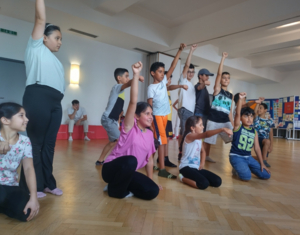 Gruppe von Kindern steht in Endpose einer Tanzperformance, strecken Hände in die Luft, knien am Boden