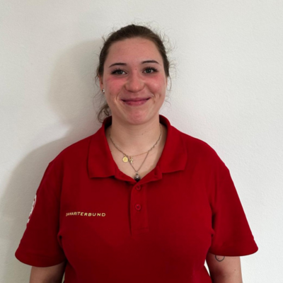 Aschaber Eine Frau mit einem roten Poloshirt lächelt vor einer weißen Wand.