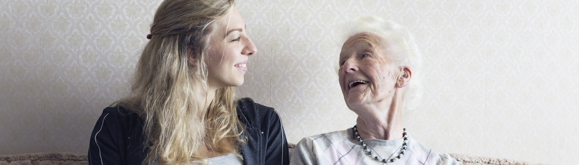 Enkelin und Oma sitzen auf Bank und lachen sich gegenseitig an