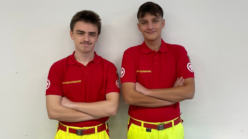 Zwei junge Männer in roten Shirts stehen nebeneinander und lächeln.