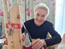 Ältere Frau bastelt Weihnachtsdekoration mit verschiedenen Materialien und Lächeln.