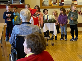 Kinder singen und stehen vor älteren Menschen in Rollstühlen.