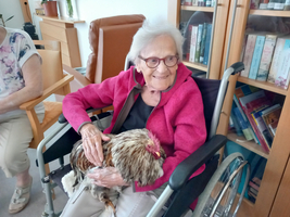 Eine ältere Frau hält ein Huhn auf ihrem Schoß und lächelt.