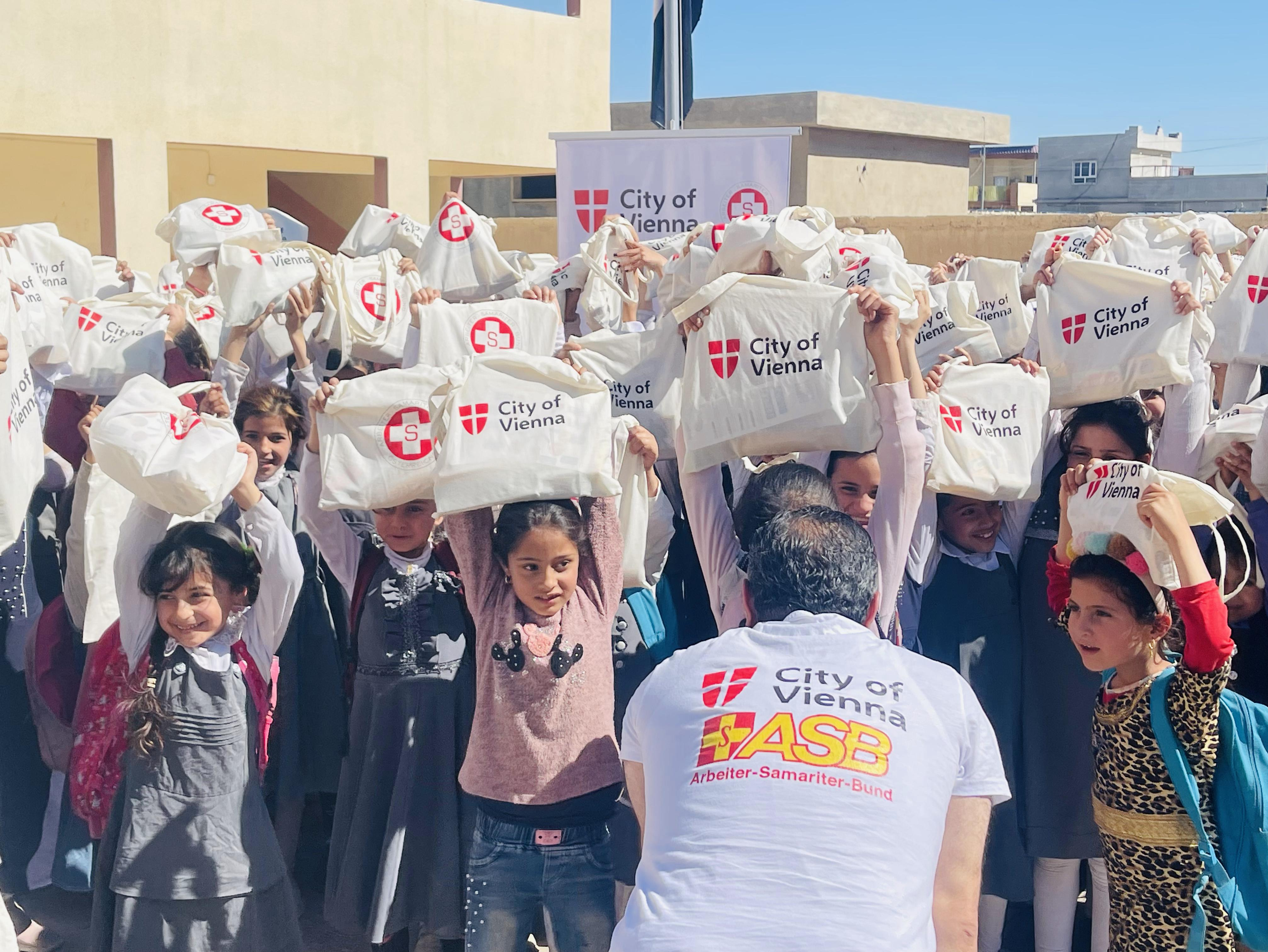 Mädchen der Schule im Irak halten Hilfspakete freudig in die Höhe