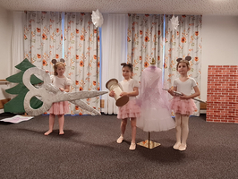 Drei Mädchen in rosa Tutu-Kleidern präsentieren Kostüme auf einer Bühne.