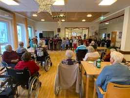 Kinder singen für Senioren in einem Gemeinschaftsraum. Feierliche Stimmung.