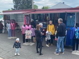 Marktstand mit Kleidung und mehreren Personen, die miteinander sprechen und einkaufen.