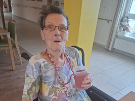 Ältere Frau im Rollstuhl, hält einen Becher in der Hand, lächelt überrascht.