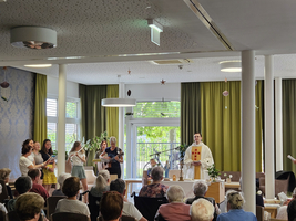 Eine Gruppe singt im Raum, während ein Priester ihnen zuhört.