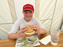 Ein Junge lächelt und hält einen Hamburger in der Hand.