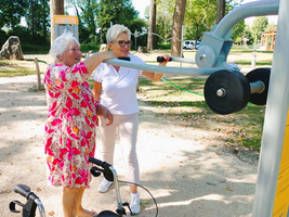 Zwei Frauen benutzen gemeinsam ein Fitnessgerät im Freien.