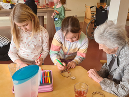 Kinder und eine ältere Frau gestalten gemeinsam kreative Bastelarbeiten am Tisch.