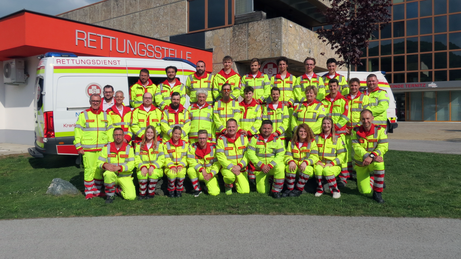 Gruppenfoto von Rettungsdienstmitarbeitern in leuchtend gelben Uniformen vor einem Rettungswagen.