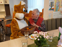 Ein Mensch im Tierkostüm sitzt mit einer älteren Dame und einem Korb voller Früchte.
