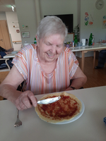 Eine lächelnde ältere Frau isst einen Pfannkuchen mit Marmelade.