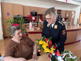 Eine Frau in Uniform überreicht einer Seniorin einen bunten Blumenstrauß.