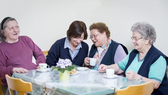 Drei Bewohnerinnen eines Pflegekompetenzzentrums beim Kaffeetrinken mit Betreuerin