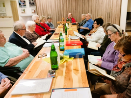 Eine Gruppe älterer Menschen sitzt an einem Tisch und liest Bücher.