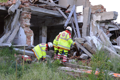 Drei Rettungseinsatzkräfte stehen vor einem zerstörten Haus. 
