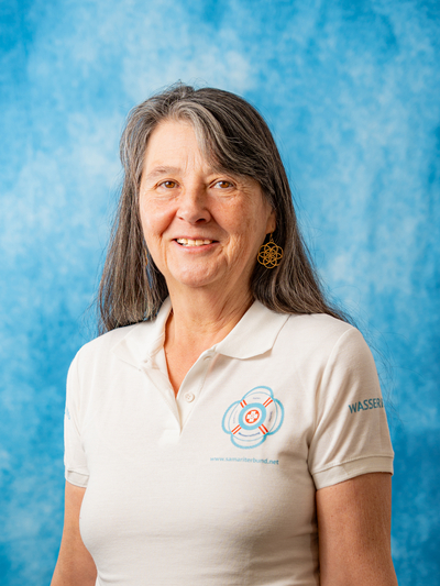Eine lächelnde Frau mit langen grauen Haaren trägt ein Poloshirt.