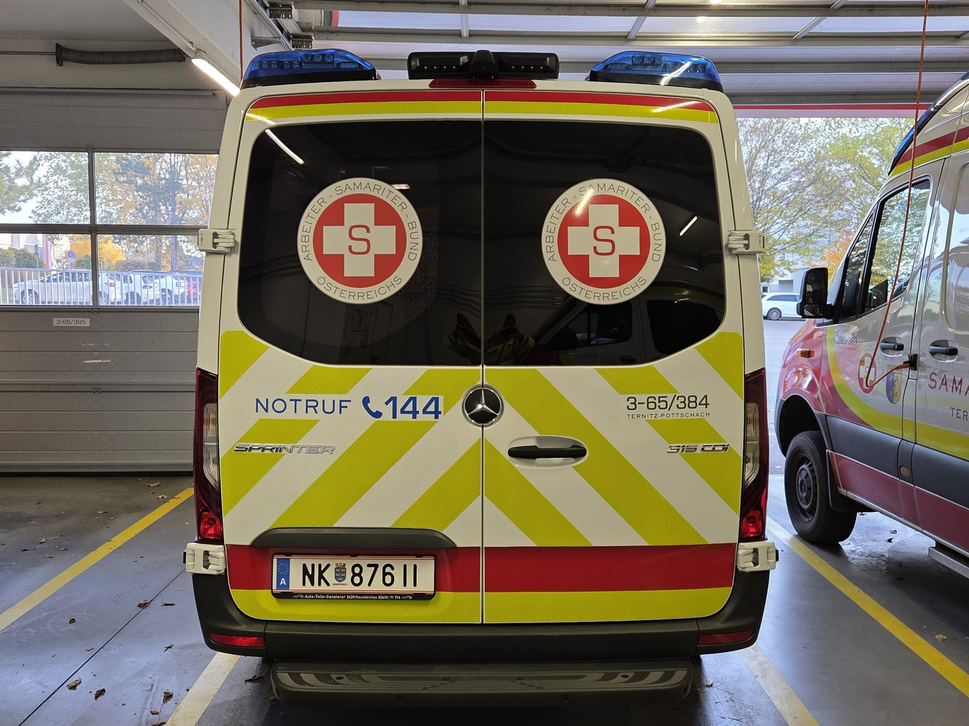 Rettungswagen mit reflektierenden Streifen und Notrufnummer 144 hinten sichtbar.