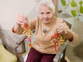 Eine ältere Frau hält zwei dekorierte Schnüre mit selbstgemachten Weihnachtsbaumornamenten.