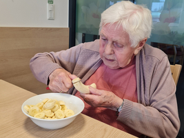 Eine ältere Frau schält eine Banane neben einer Schüssel mit aufgeschnittenen Bananen.