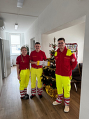 Drei Einsatzkräfte in uniform stehen vor einem Weihnachtsbaum und halten Geschenke.