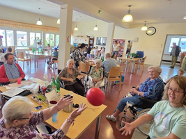 Senioren und Jugendliche spielen gemeinsam mit einem roten Ball in einem Gemeinschaftsraum.