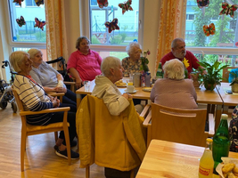 Eine Gruppe älterer Menschen sitzt an einem Tisch und hört zu.
