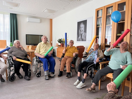Ältere Menschen sitzen mit bunten Schwimmnudeln und schauen nach oben.