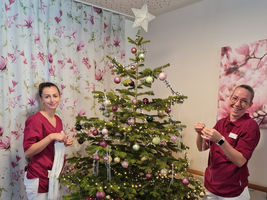 Zwei Pflegekräfte dekorieren einen festlich geschmückten Weihnachtsbaum.