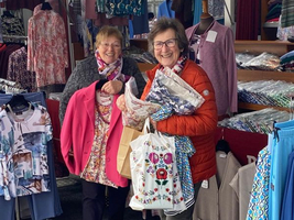 Zwei Frauen lächeln und halten Einkaufstaschen mit Kleidung in einem Stand.
