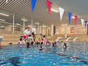 Schwimmtrainer gibt Anweisungen an Schwimmerinnen im Becken, umgeben von Schwimmflaggen.