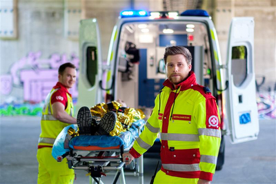 Zwei Sanitäter in Uniform transportieren eine Trage mit einer Person im Rettungswagen.